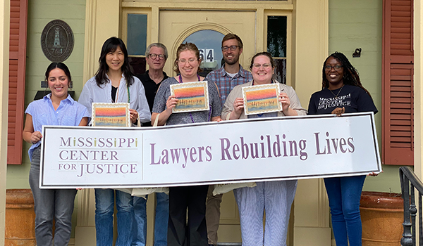 A Spring Break Pro Bono Trip to Mississippi, Students posing with a sign that says "Mississippi Center for Justice, Lawyers Rebuilding Lives"